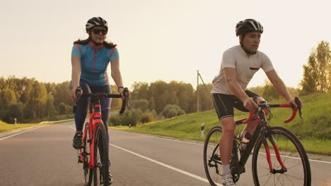 Steadicam-shot-of-mountain-biking-couple-riding-on-bike-trail-at-sunset-doing-high.